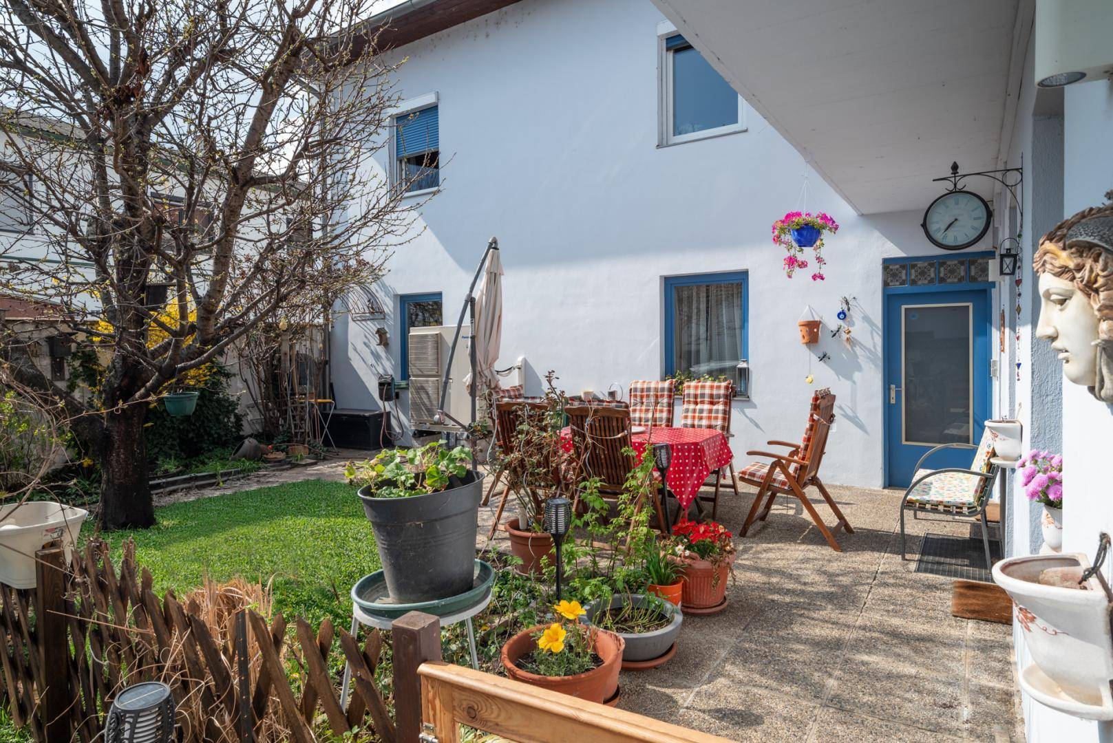 Gemütlicher Gartenbereich mit Sitzgelegenheiten, Pflanzen und einem Baum.