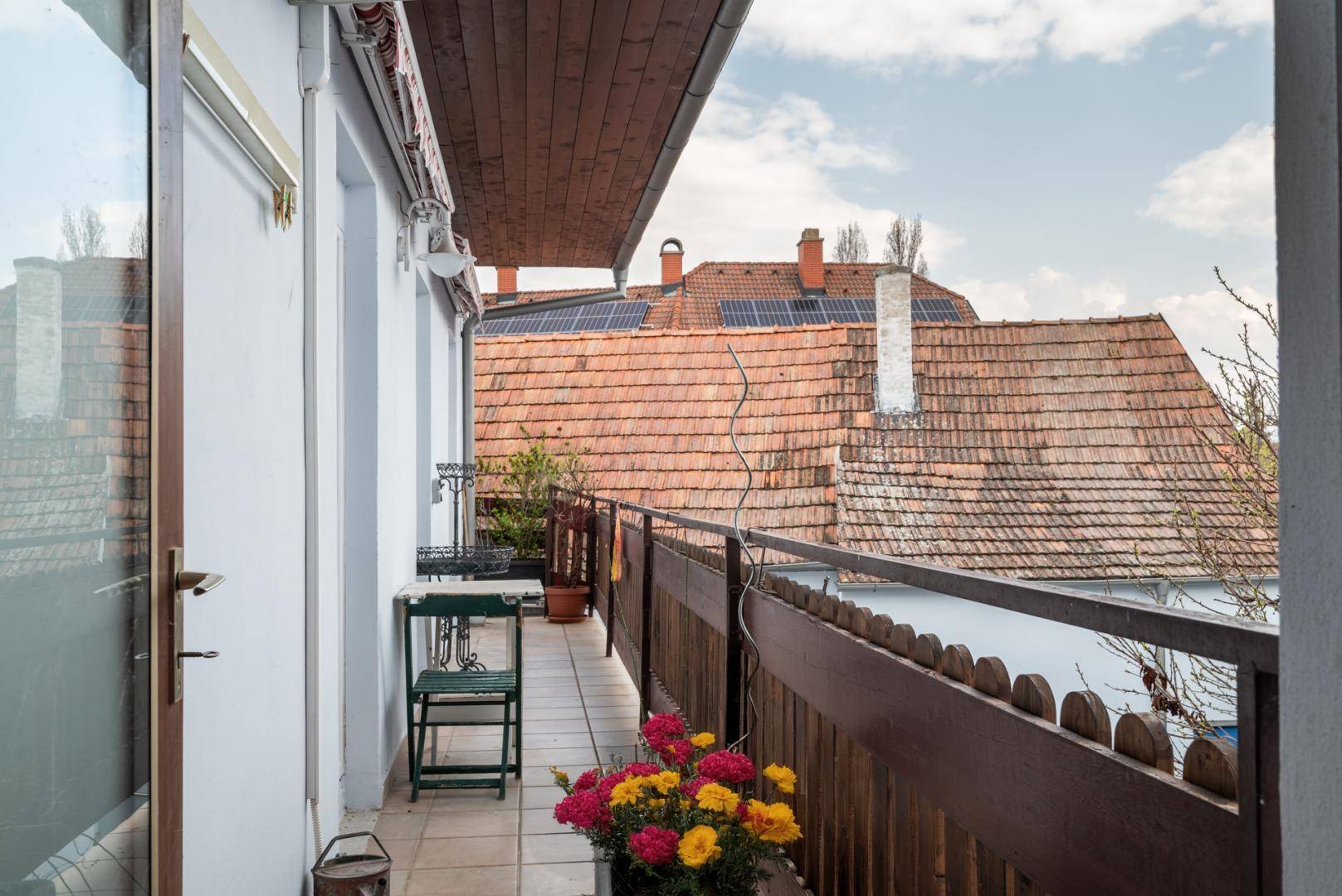 Schmaler Balkon mit Fliesenboden, Blumen und Blick auf Dächer mit Solaranlagen.
