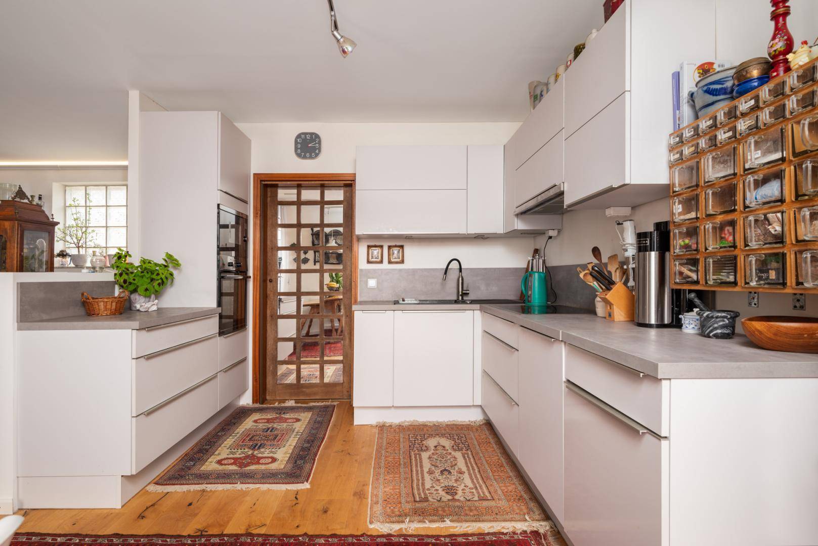 Moderne weiße Küche mit Einbaugeräten, Holzfußboden und Teppichen.