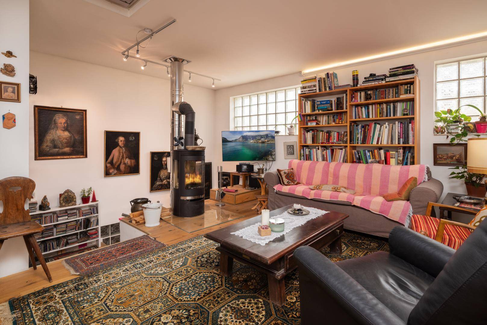 Gemütliches Wohnzimmer mit Kaminofen, Bücherregal und Teppich.
