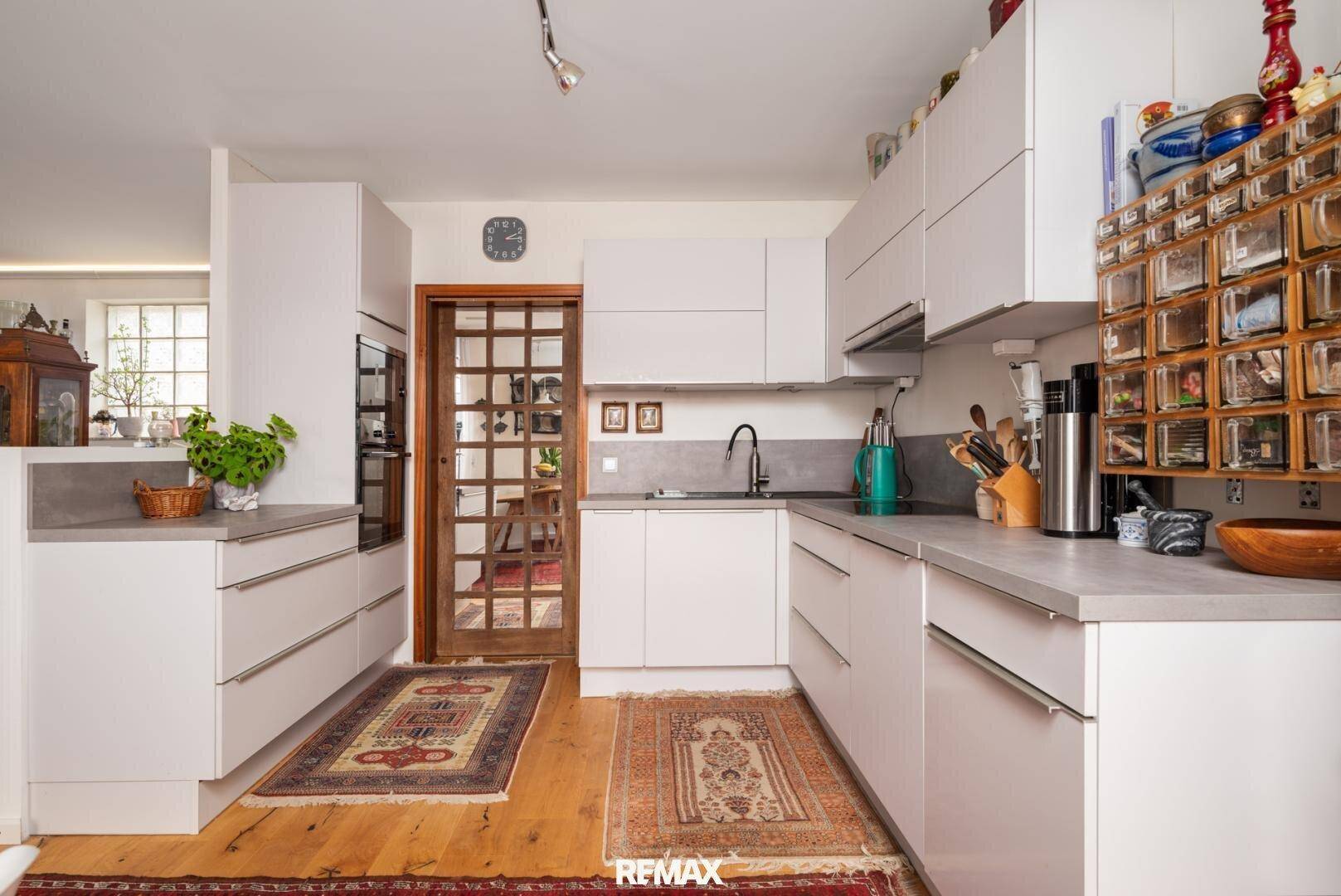 Moderne weiße Küche mit hellen Arbeitsplatten und Holzboden.