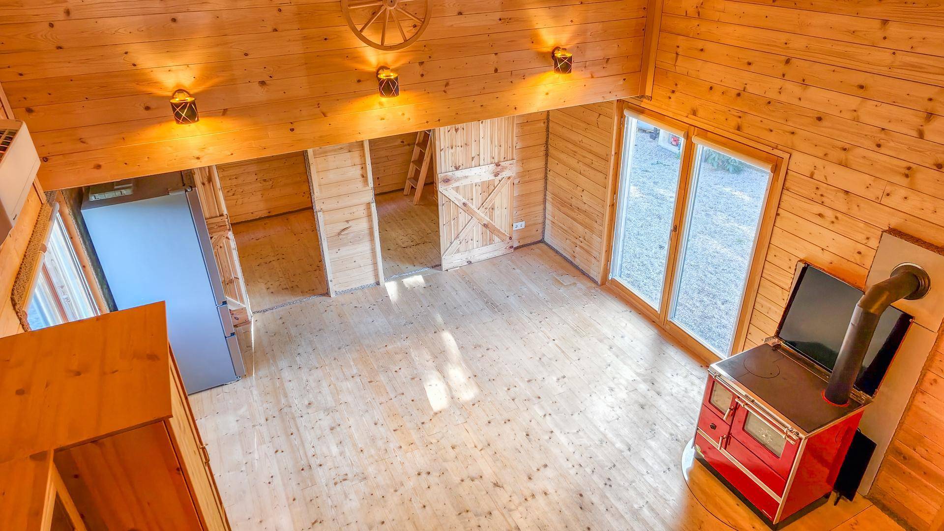 Offener Wohnbereich von oben gesehen mit Holzboden, Kaminofen und Zugang zur Terrasse.
