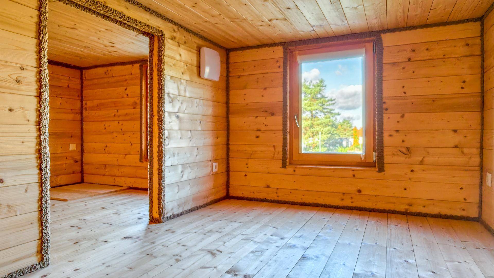 Helles Zimmer mit Holzvertäfelung, Holzboden und einem großen Fenster mit Ausblick ins Grüne.