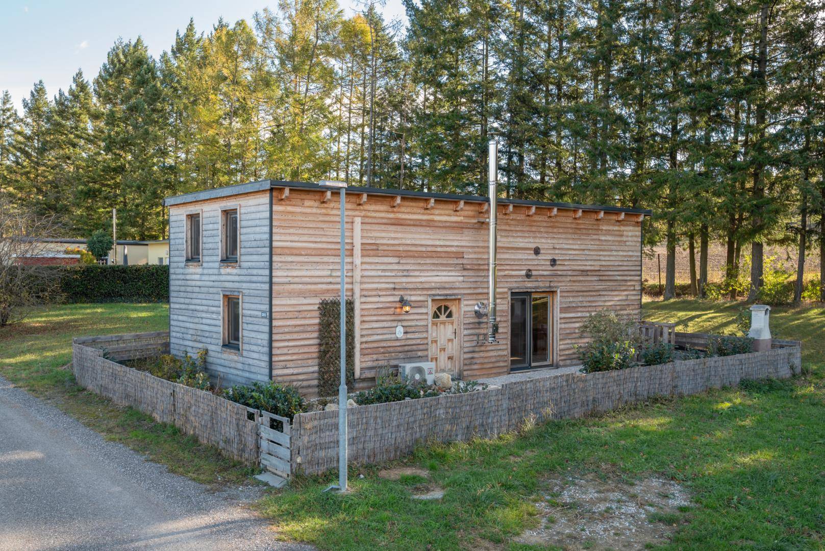 Freistehendes Holzhaus mit einfacher Architektur und umzäuntem Vorgartenbereich in grüner Umgebung.