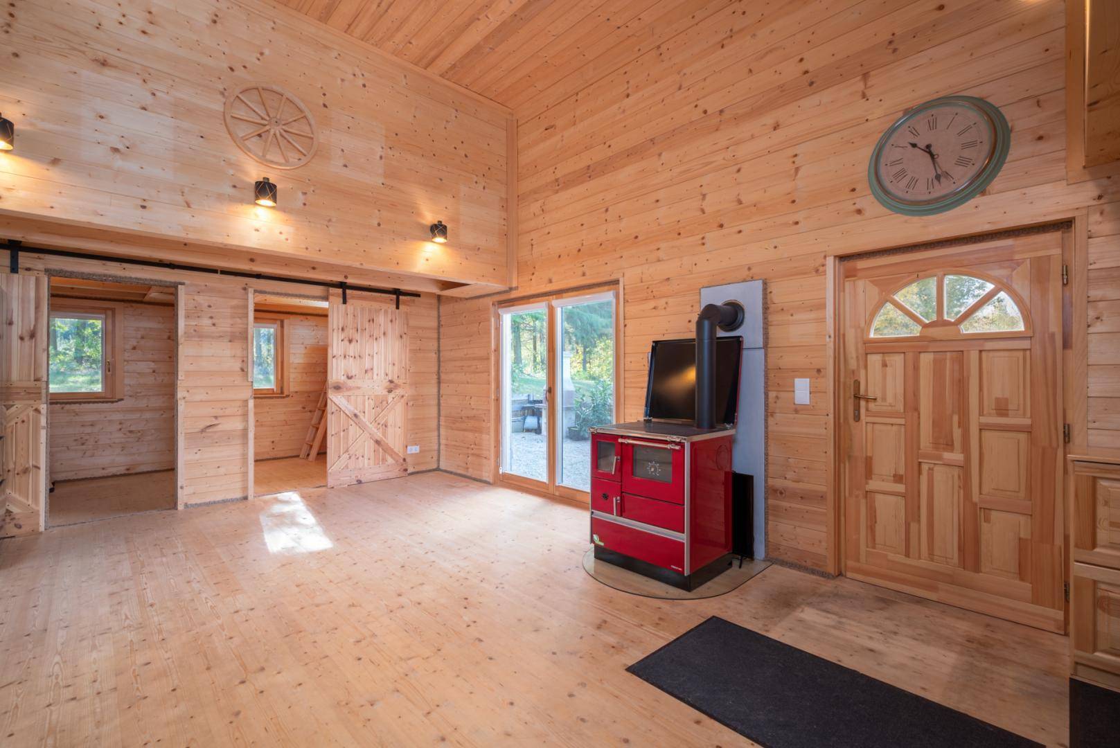 Geräumiges Wohnzimmer mit Holzboden, Holzvertäfelung und einem roten Kaminofen als Blickfang.