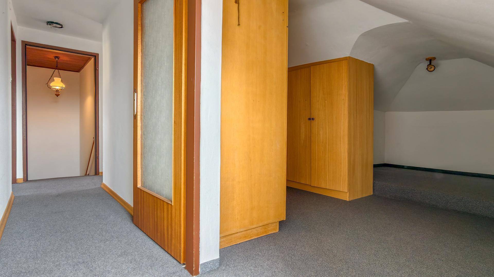 Flur im Dachgeschoss mit Teppichboden und Holzschränken, der zu weiteren Räumen führt.