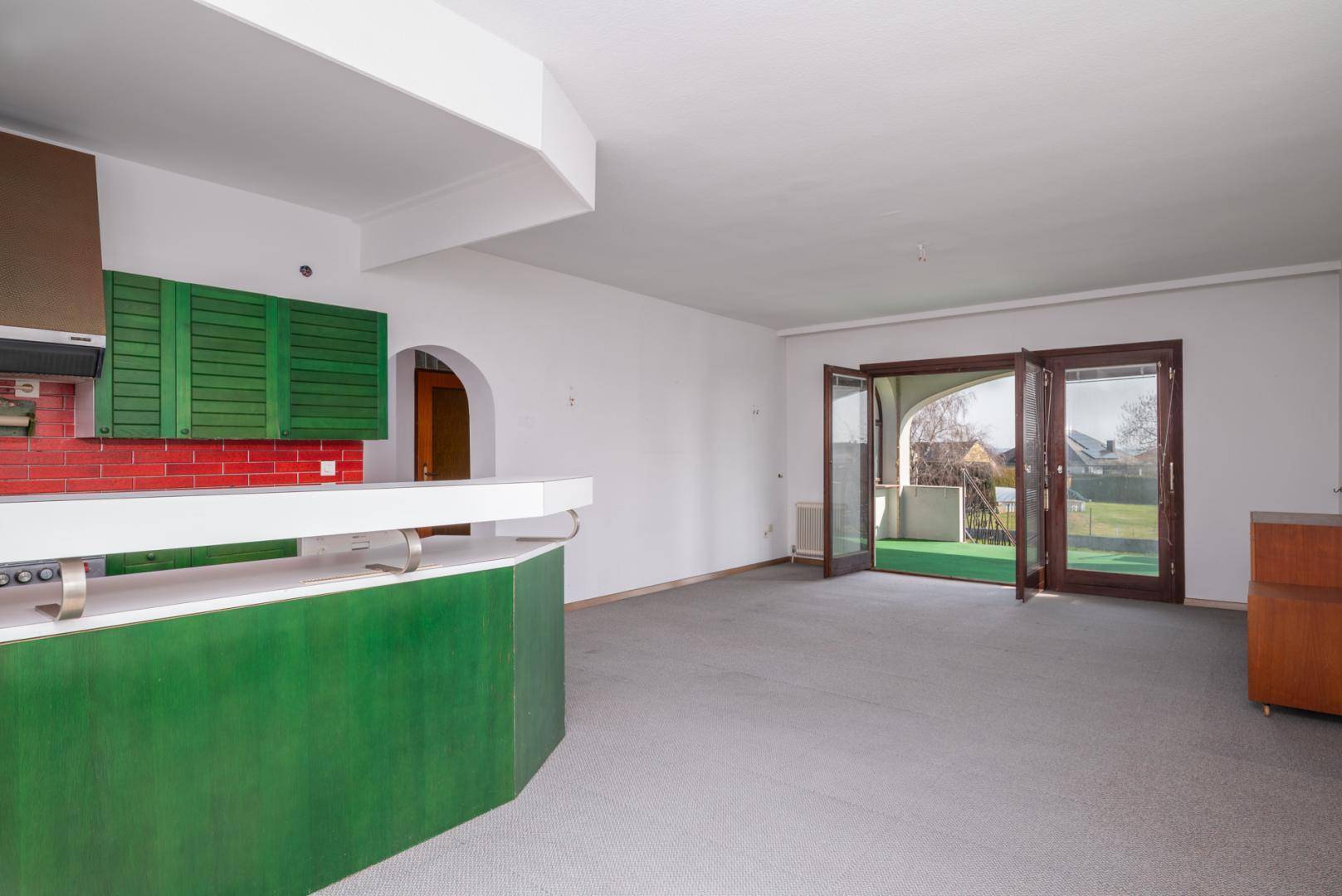 Heller Wohnbereich mit Teppichboden und Zugang zu einer überdachten Terrasse oder Loggia.