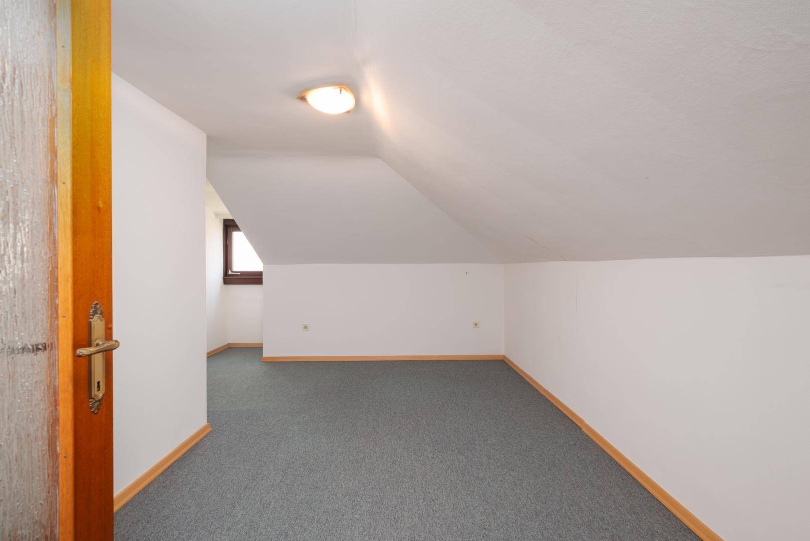 Weiterer Raum im Dachgeschoss mit Teppichboden und schrägen Wänden, ideal als Schlaf- oder Arbeitszimmer.