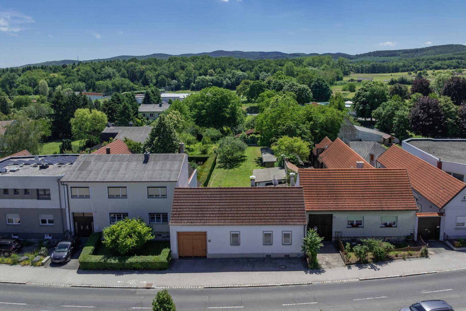 Luftaufnahme des Hauses mit umliegenden Gärten und einer weiten grünen Landschaft im Hintergrund.