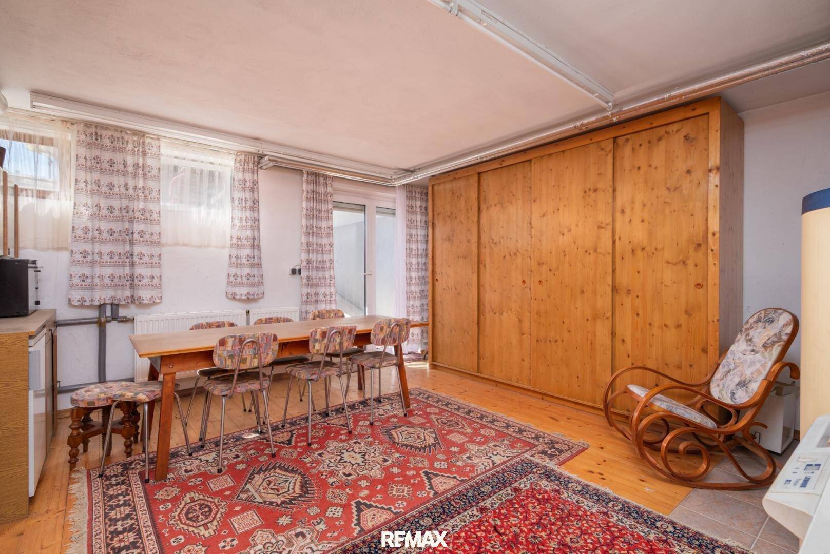 Geräumiger Mehrzweckraum mit großem Esstisch, Holzschrank und Zugang zum Außenbereich.