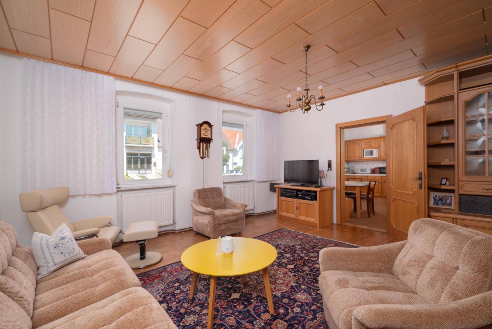 Gemütliches Wohnzimmer mit bequemen Sitzmöbeln, einem Fernseher und einer warmen Holzpaneeldecke.