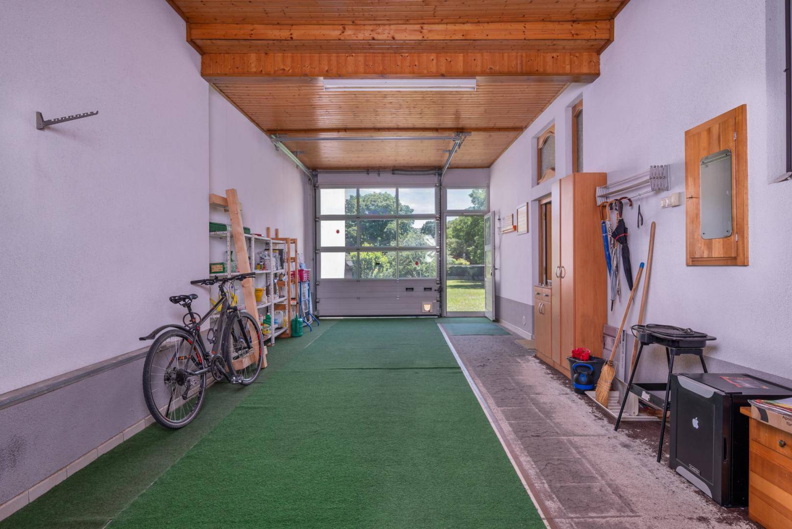 Geräumige Garage mit grünem Teppich, Fahrrädern und Regalen, mit Zugang zum Garten.