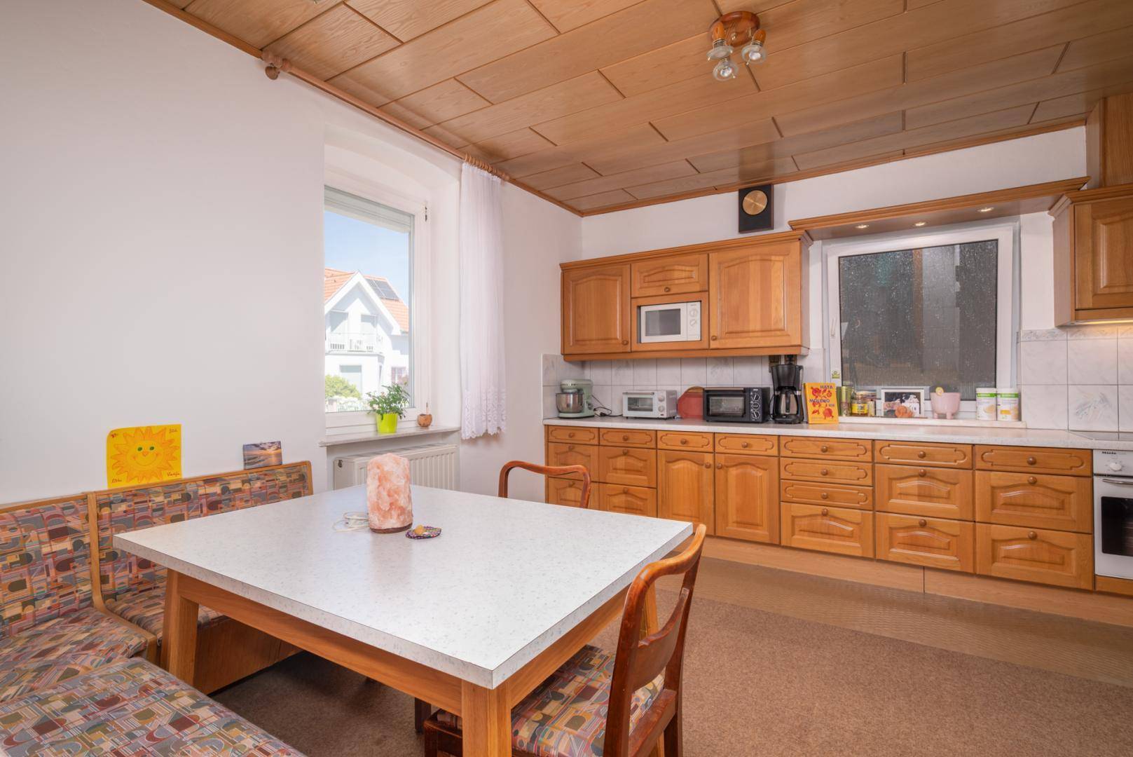 Geräumige Wohnküche mit Holzschränken, einem Esstisch mit Eckbank und einem Fenster für Tageslicht.