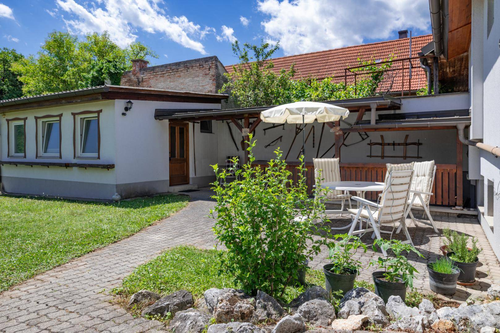 Gemütliche Terrasse mit Gartenmöbeln und Sonnenschirm, umgeben von Grünflächen und einem gepflasterten Weg.