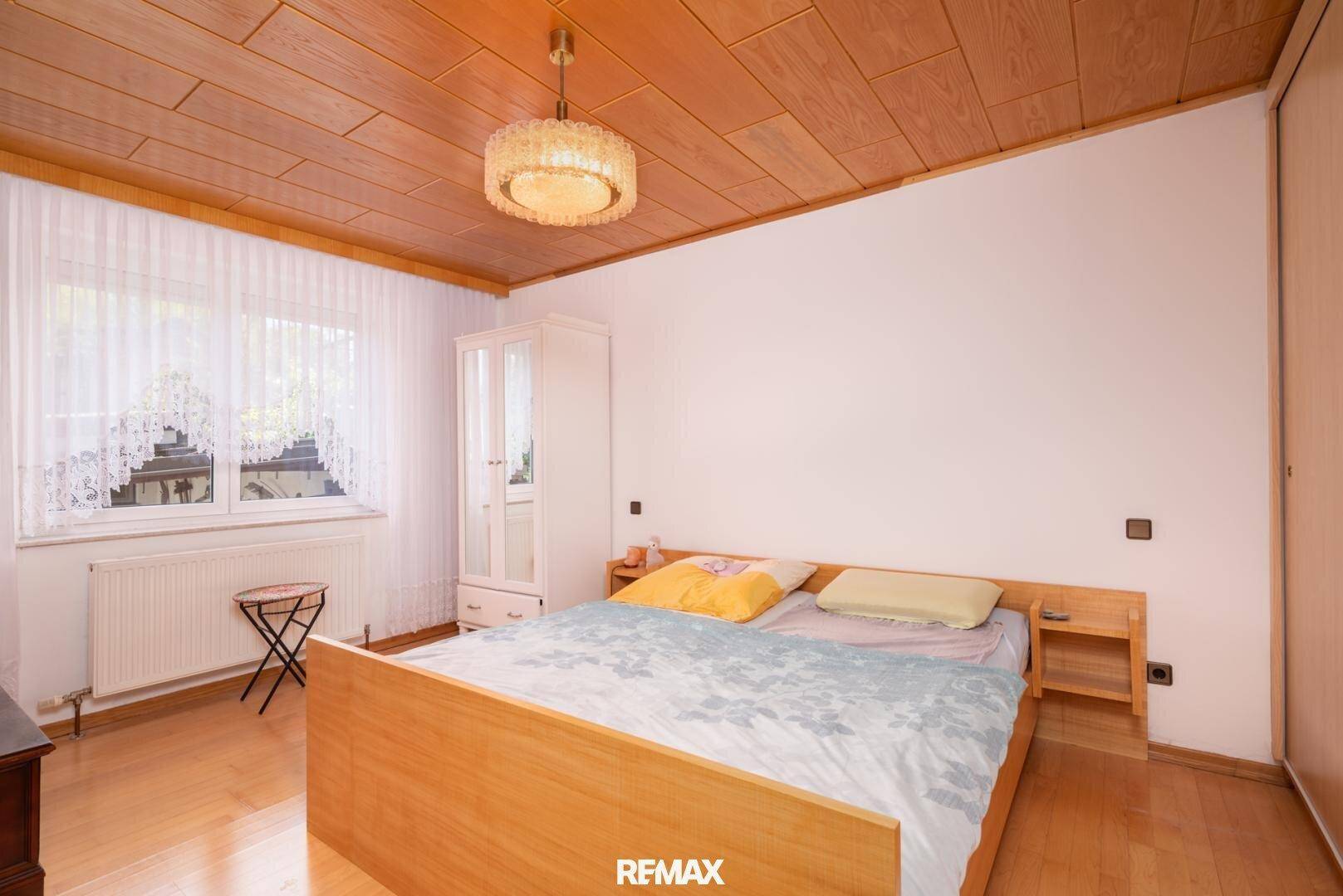 Schlafzimmer mit Doppelbett, Kleiderschrank und einer warmen Holzdeckenverkleidung.