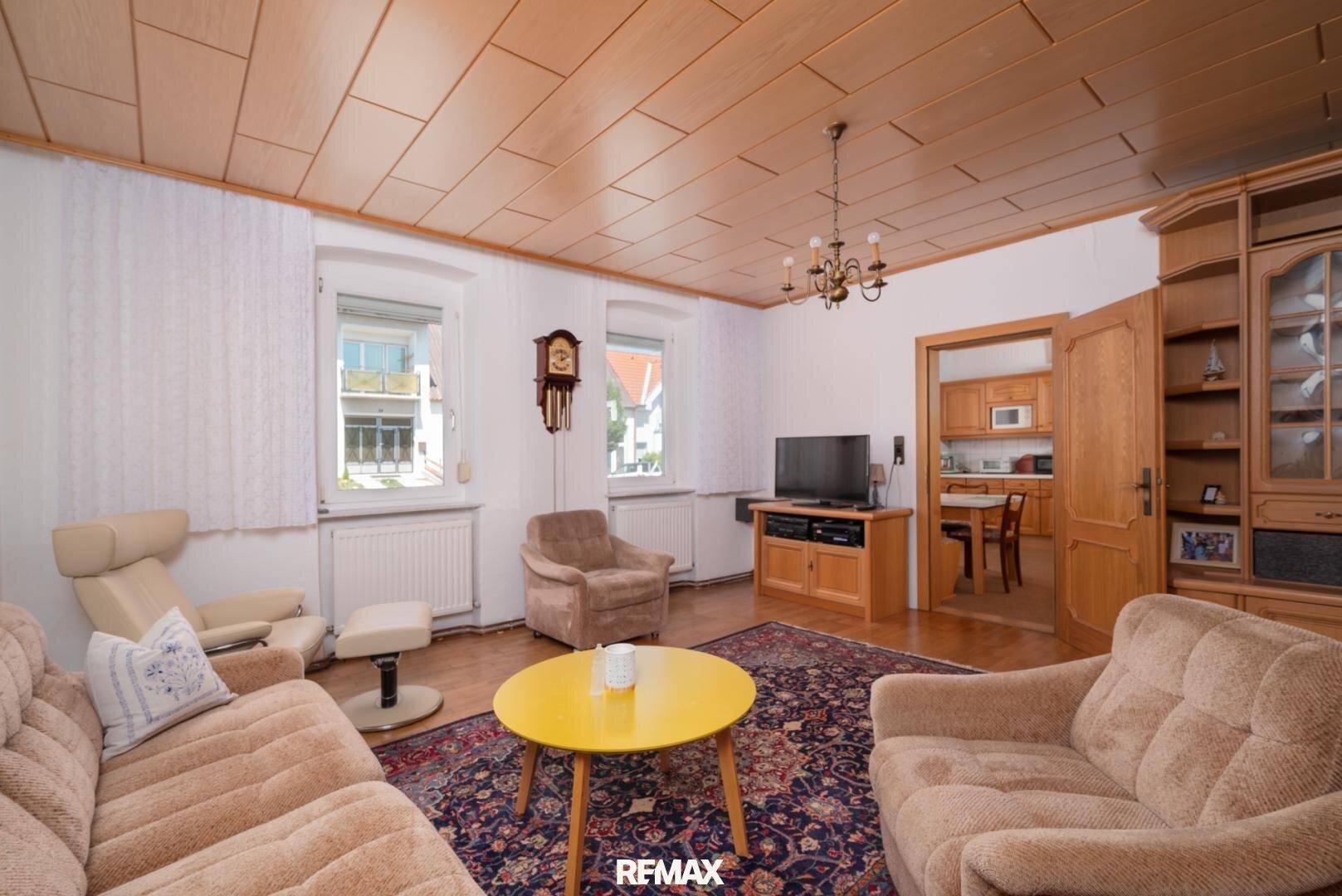 Gemütliches Wohnzimmer mit traditionellen Möbeln, Holzdecke und Durchgang zur Küche.