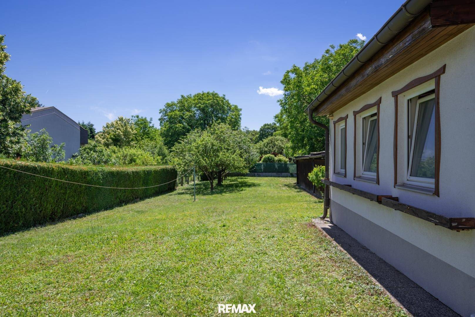 Seitlicher Blick auf das Haus und den weitläufigen Garten mit gepflegtem Rasen und Hecke.