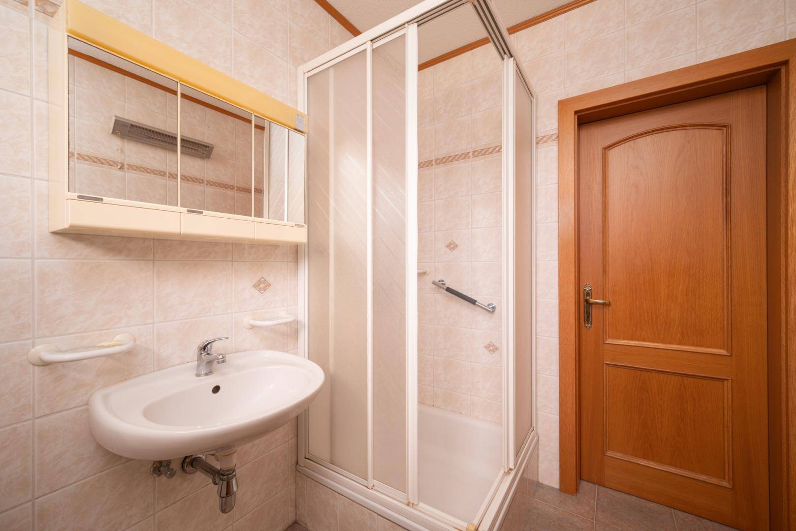 Funktionales Badezimmer mit hellen Fliesen, einem Waschbecken und einer Duschkabine.