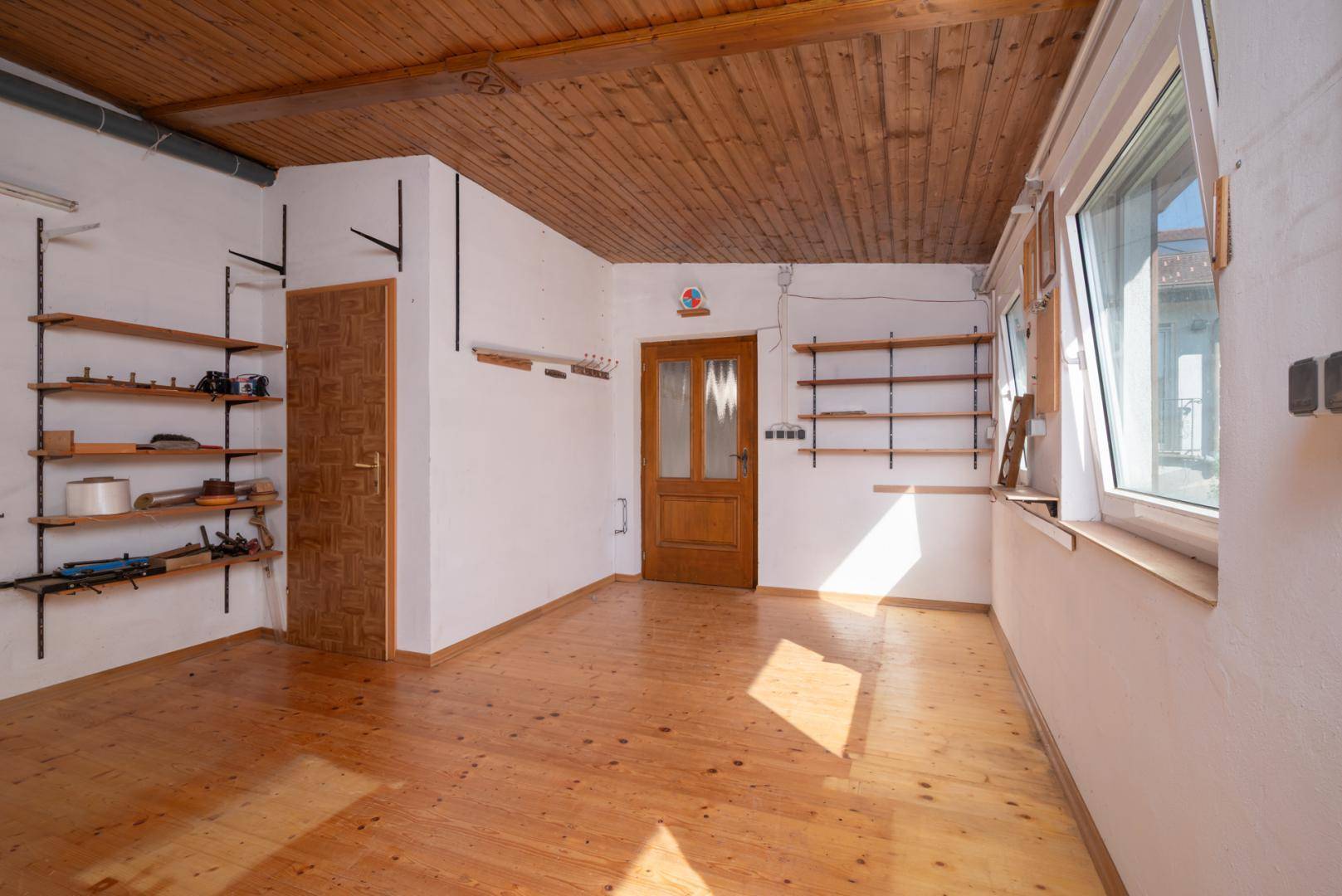 Heller Raum mit Holzfußboden, Holzpaneeldecke und Regalen an den Wänden, vielseitig nutzbar.
