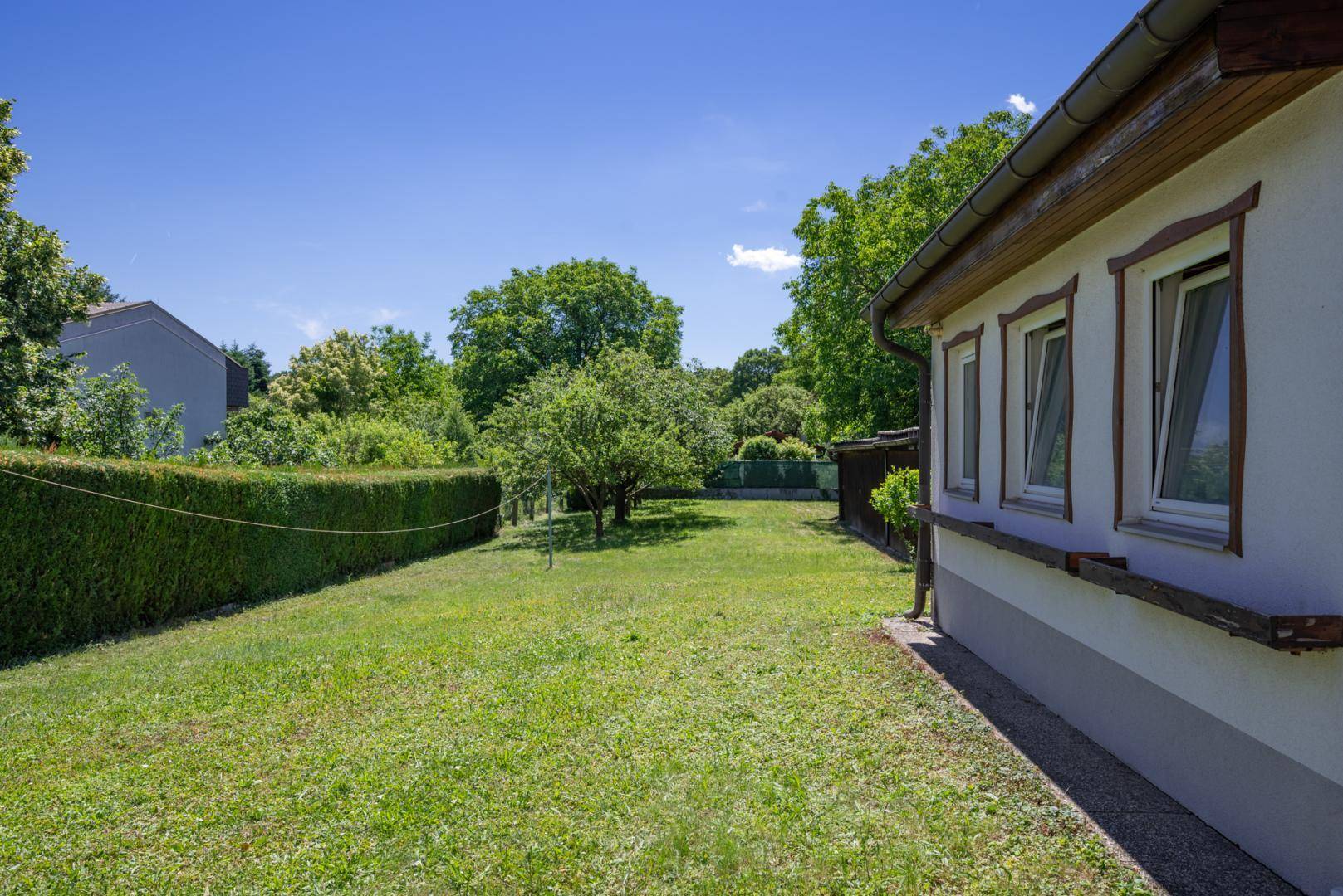 Seitenansicht des Hauses mit einer weitläufigen Rasenfläche und einer gepflegten Hecke.