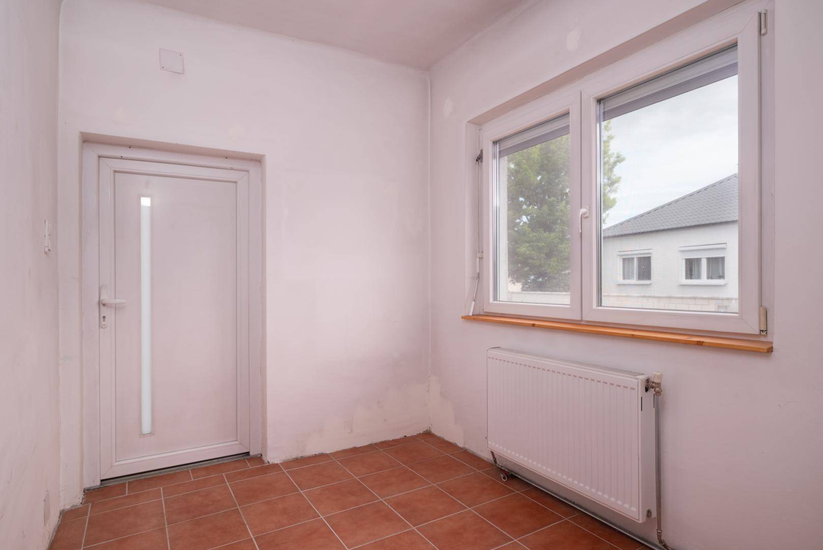Kleiner Flur oder Eingangsbereich mit Terrakotta-Fliesenboden, weißer Tür und Fenster.