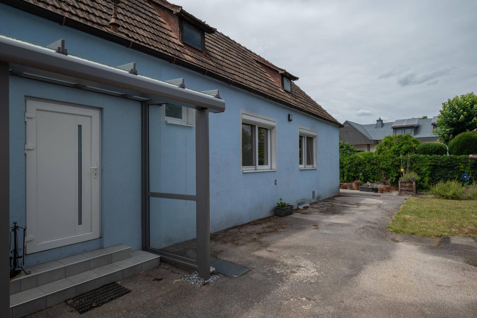 Seitenansicht des Hauses mit Eingangsbereich, überdachtem Zugang und einer gepflasterten Einfahrt.