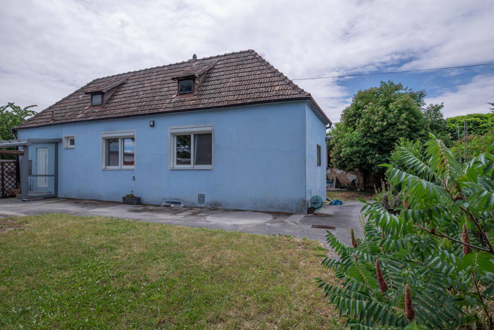 Seitenansicht des blauen Hauses vom Garten aus, mit Eingangsbereich und gepflasterter Fläche.