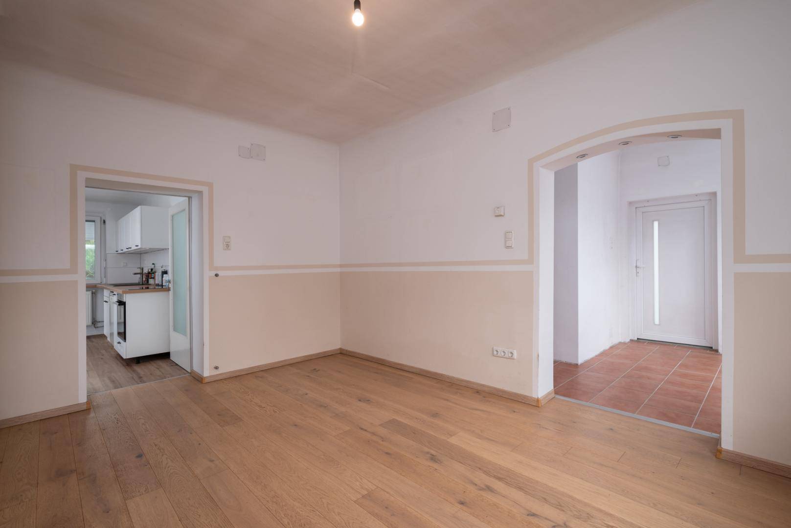 Leerer Essbereich mit Holzboden, einem Durchgang zum Flur und Blick in die Küche.