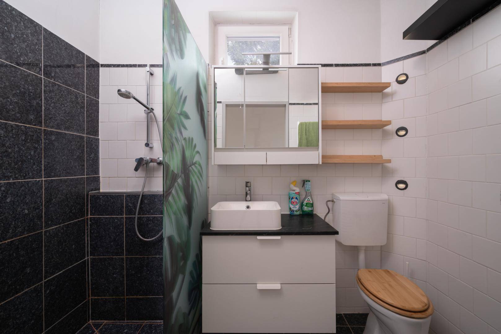 Modernes Badezimmer mit schwarz-weißen Fliesen, Dusche, Einzelwaschbecken und WC.