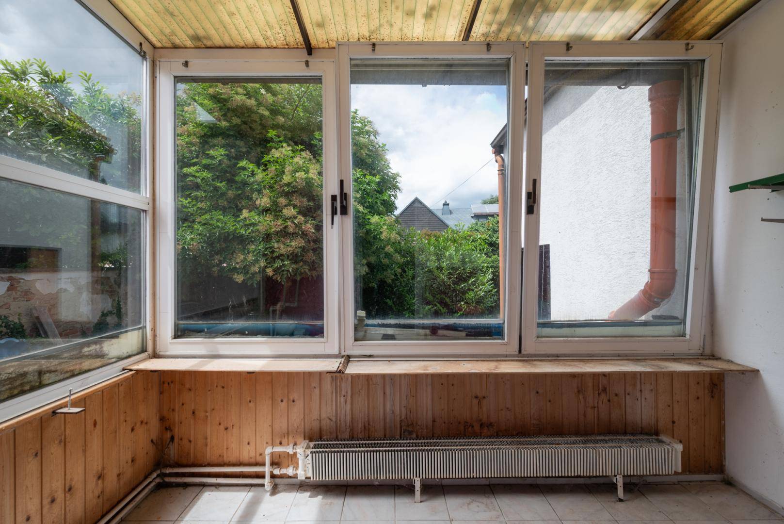 Heller Wintergarten mit großen Fenstern, Holzverkleidung und Heizkörper, bietet einen schönen Ausblick.