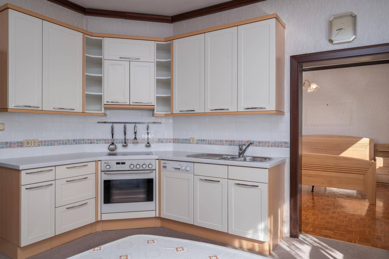 Funktionale Einbauküche mit hellen Schränken und integrierten Geräten, angrenzend an ein Schlafzimmer.