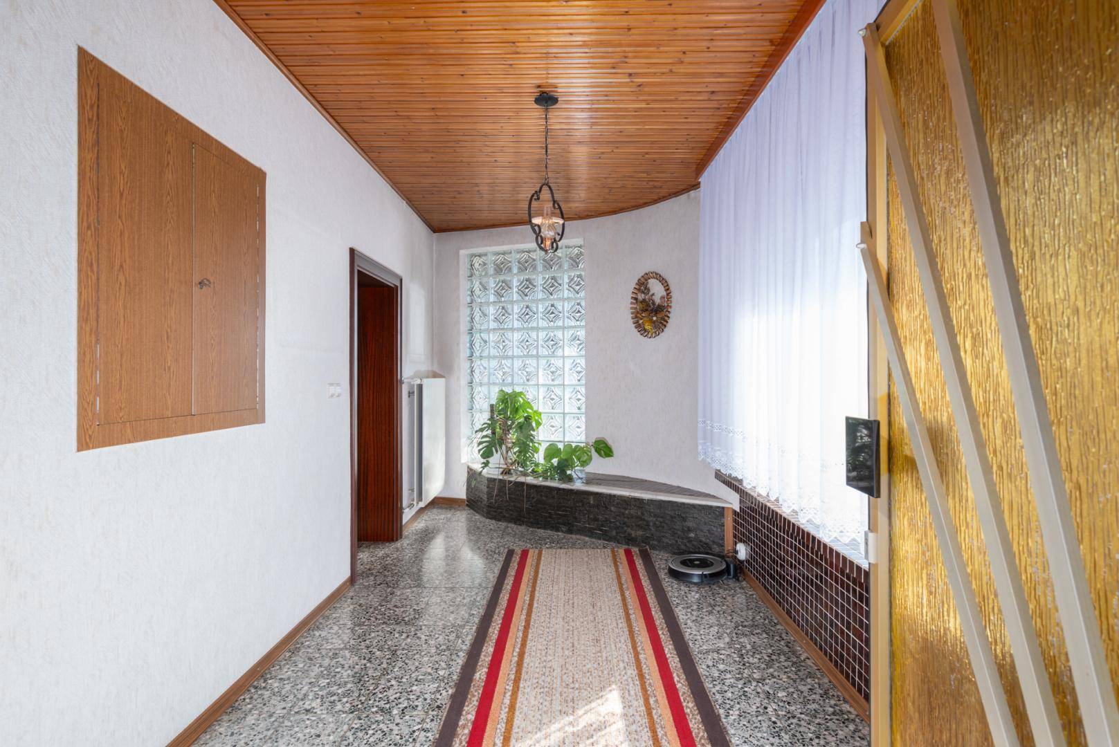 Heller Flur mit Holzdecke, Terrazzoboden und dekorativen Glasbausteinen für natürliches Licht.