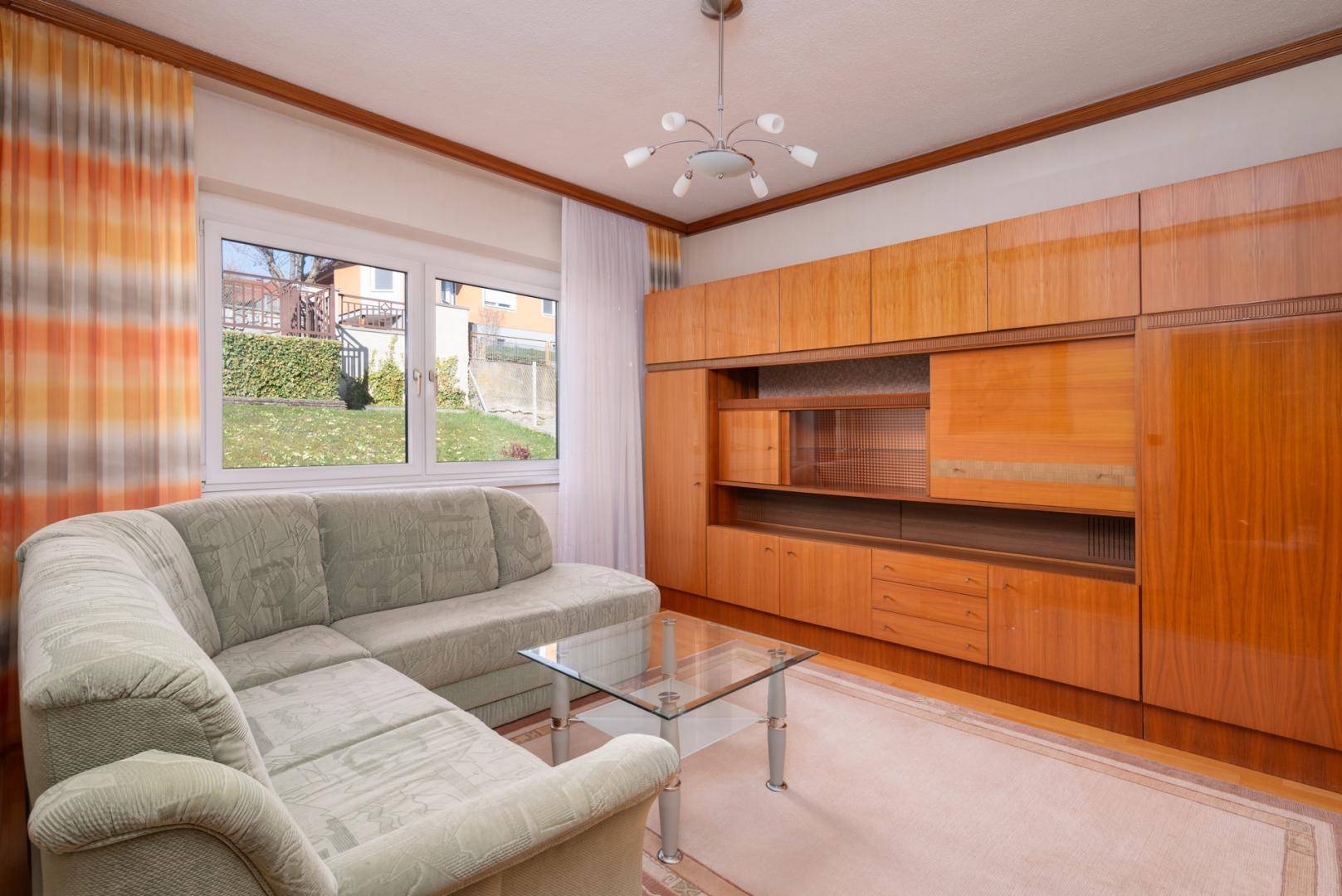 Gemütliches Wohnzimmer mit großem Sofa, Holzwandmöbeln und Blick in den Garten.