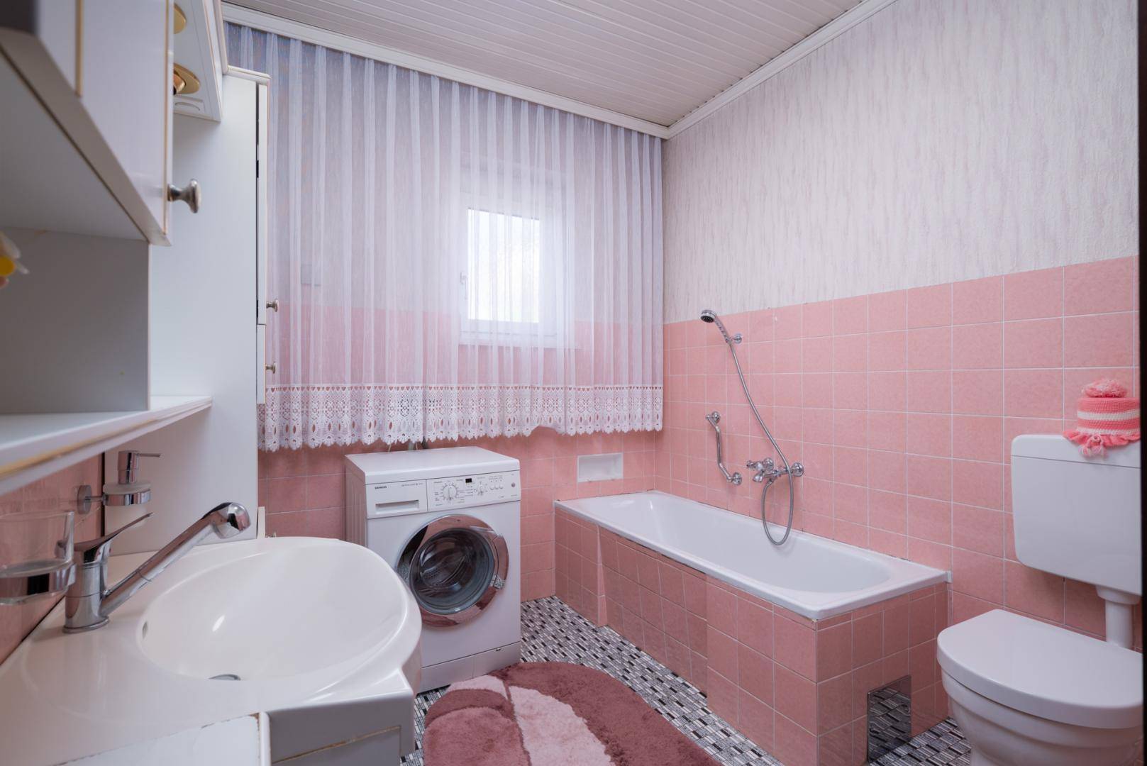 Badezimmer im 80er-Jahre-Stil mit rosa Fliesen, Badewanne und Waschmaschine.