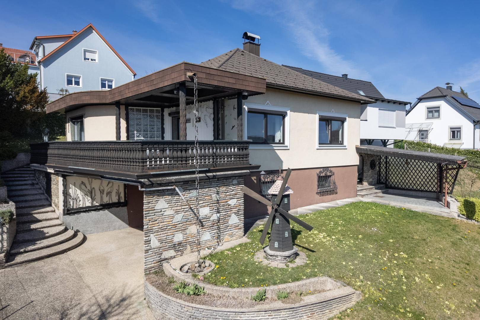 Rückseite des Hauses mit Balkon, Carport und dekorativer Windmühle im Garten.