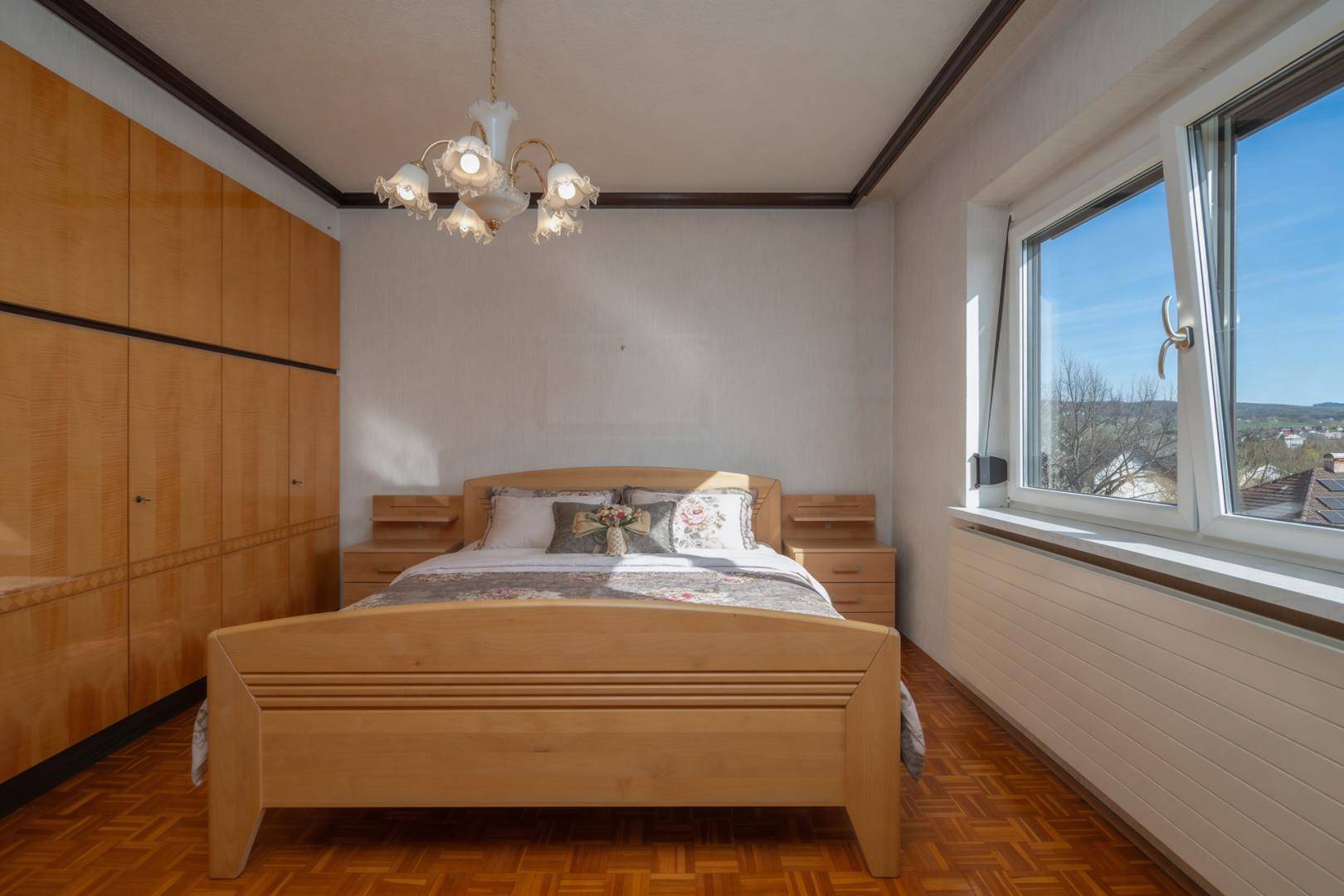 Helles Schlafzimmer mit Holzparkettboden, Doppelbett und großem Fenster mit Fernblick.