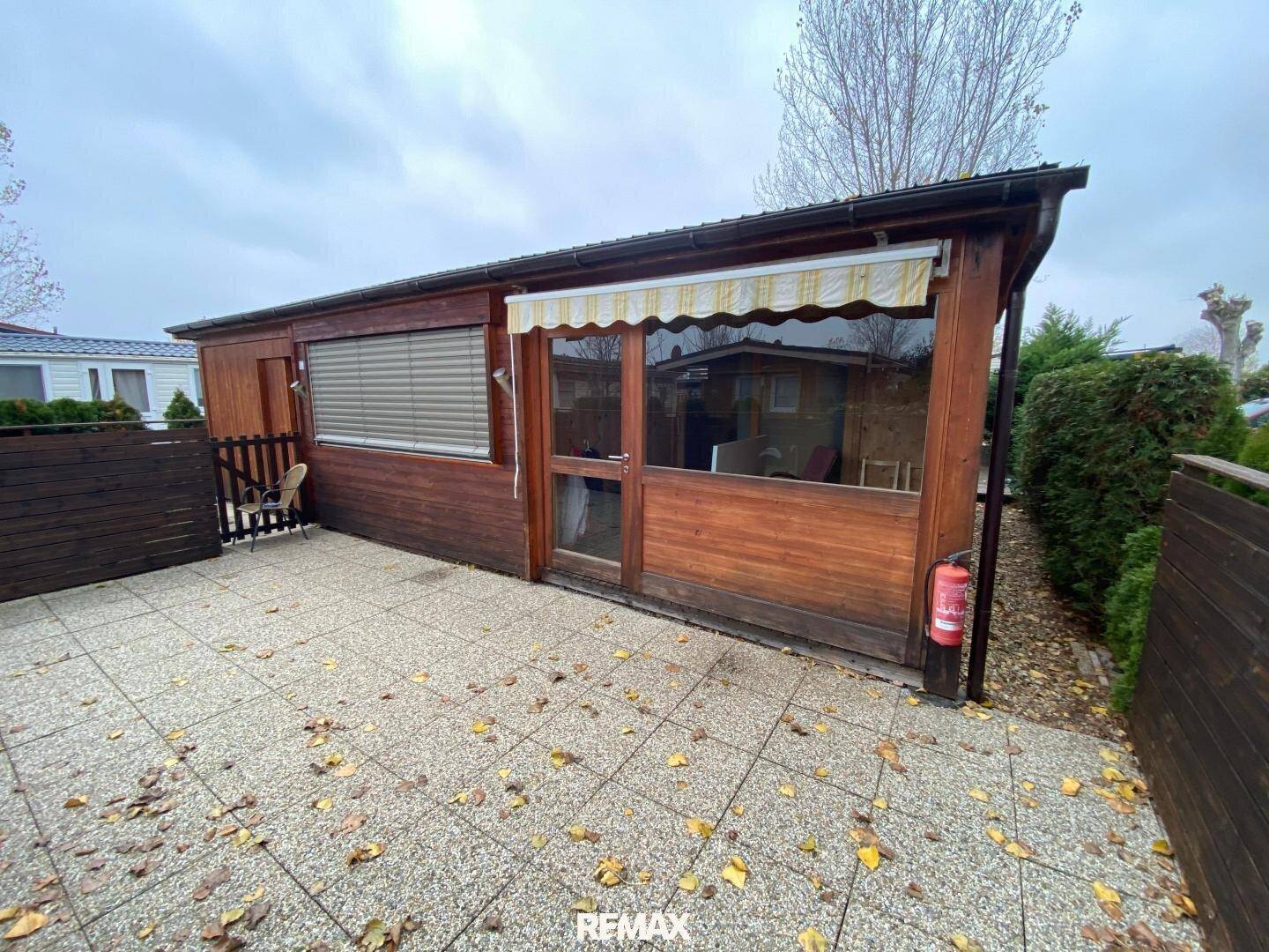 Außenansicht einer Holzhütte mit gepflasterter Terrasse und Markise.