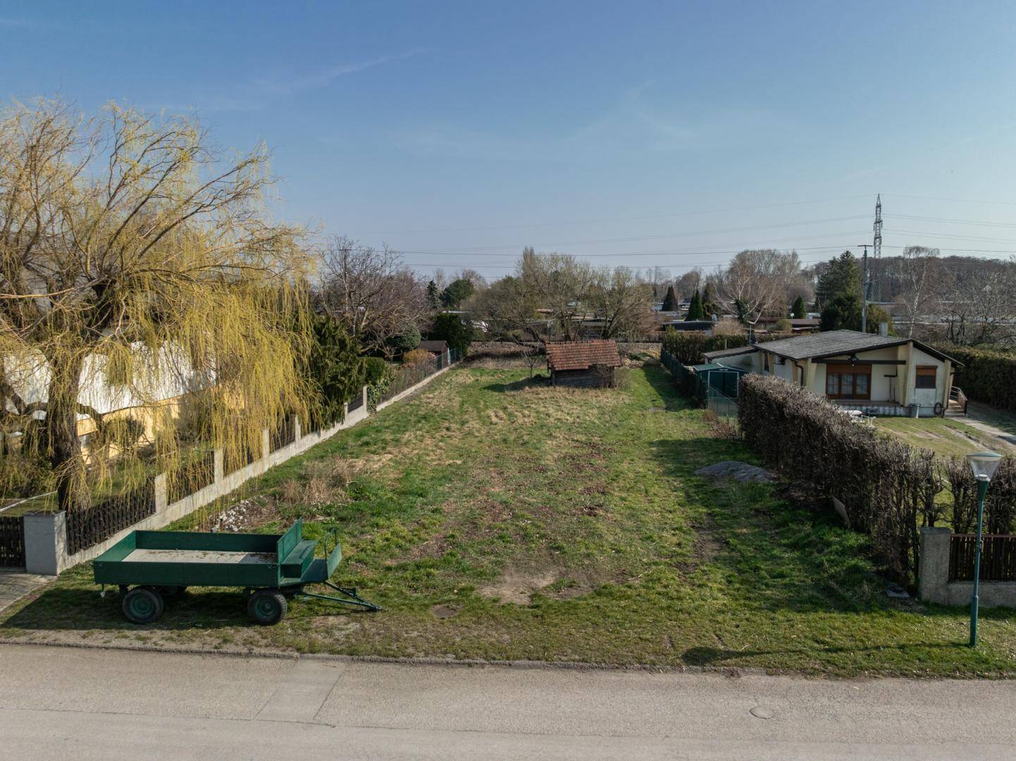 Weitläufiges Grundstück mit Rasen, kleinem Schuppen und Blick auf die umgebende Landschaft und Stromleitungen.