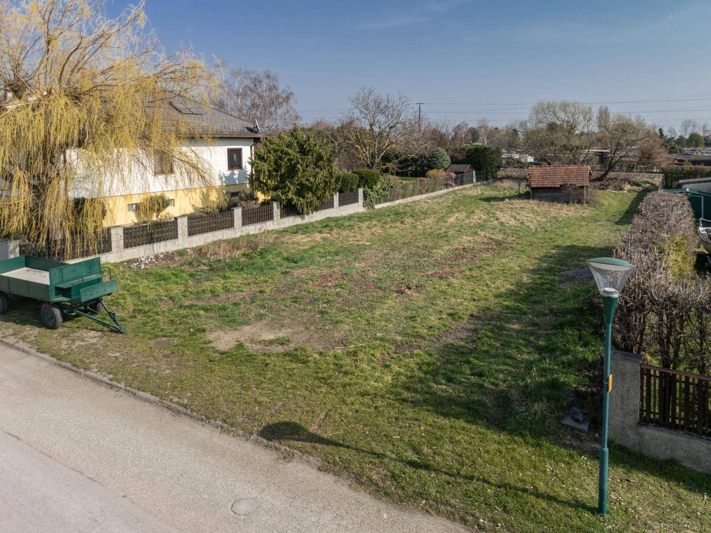 Blick auf ein unbebautes Grundstück mit Rasenfläche, einem kleinen Schuppen und angrenzender Straße.
