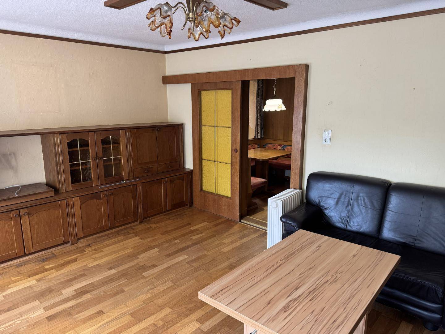 Wohnzimmer mit Holzfußboden, Ledersofa und Durchgang zu einem weiteren Raum.