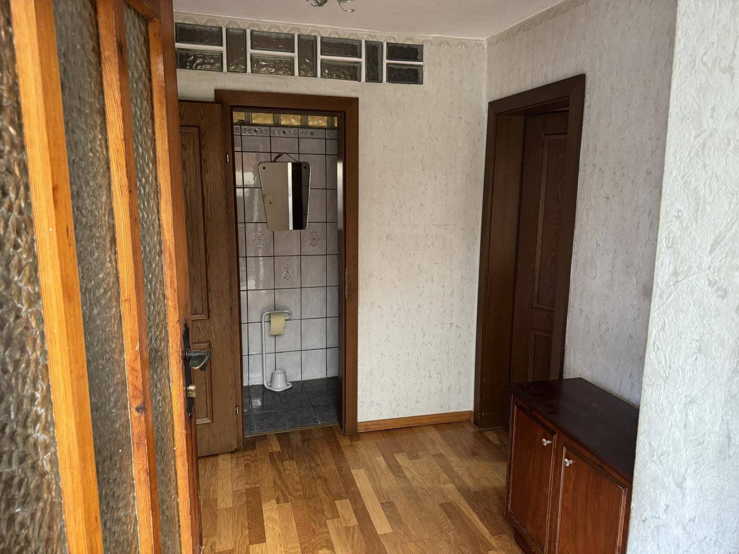 Flur mit Holzfußboden, dunklen Türen und Zugang zu einem gefliesten WC.