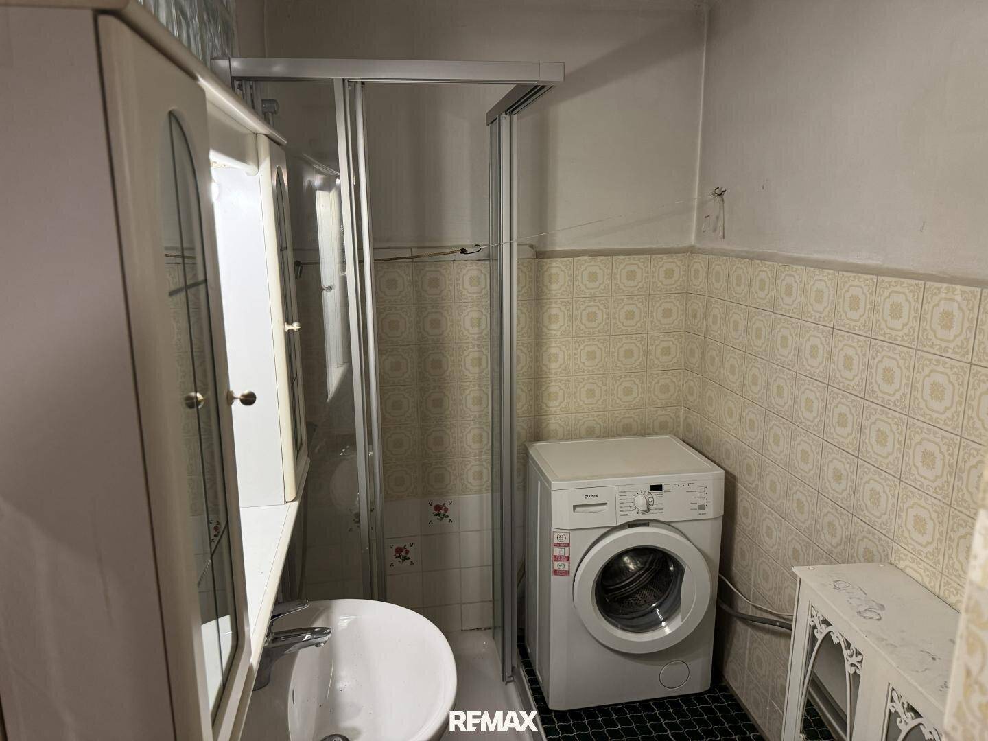 Badezimmer mit Duschkabine, Waschbecken und Waschmaschine, funktional und hell gefliest.