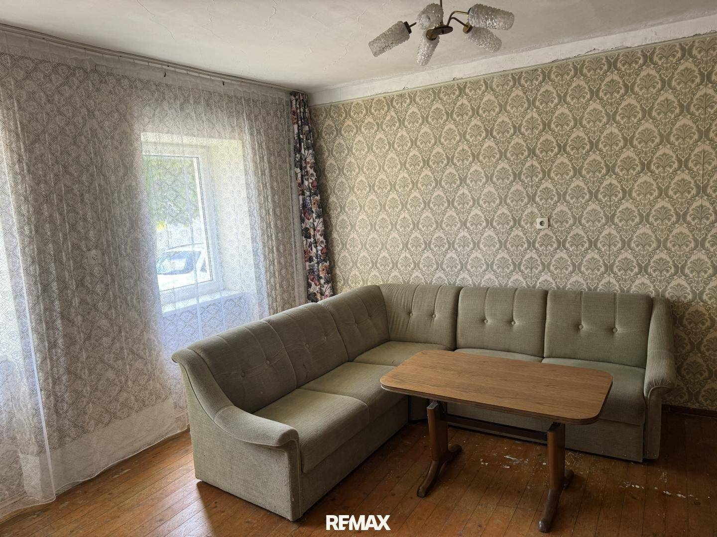 Gemütliches Wohnzimmer mit Ecksofa, Holztisch und gemusterter Tapete, strahlt traditionellen Charme aus.