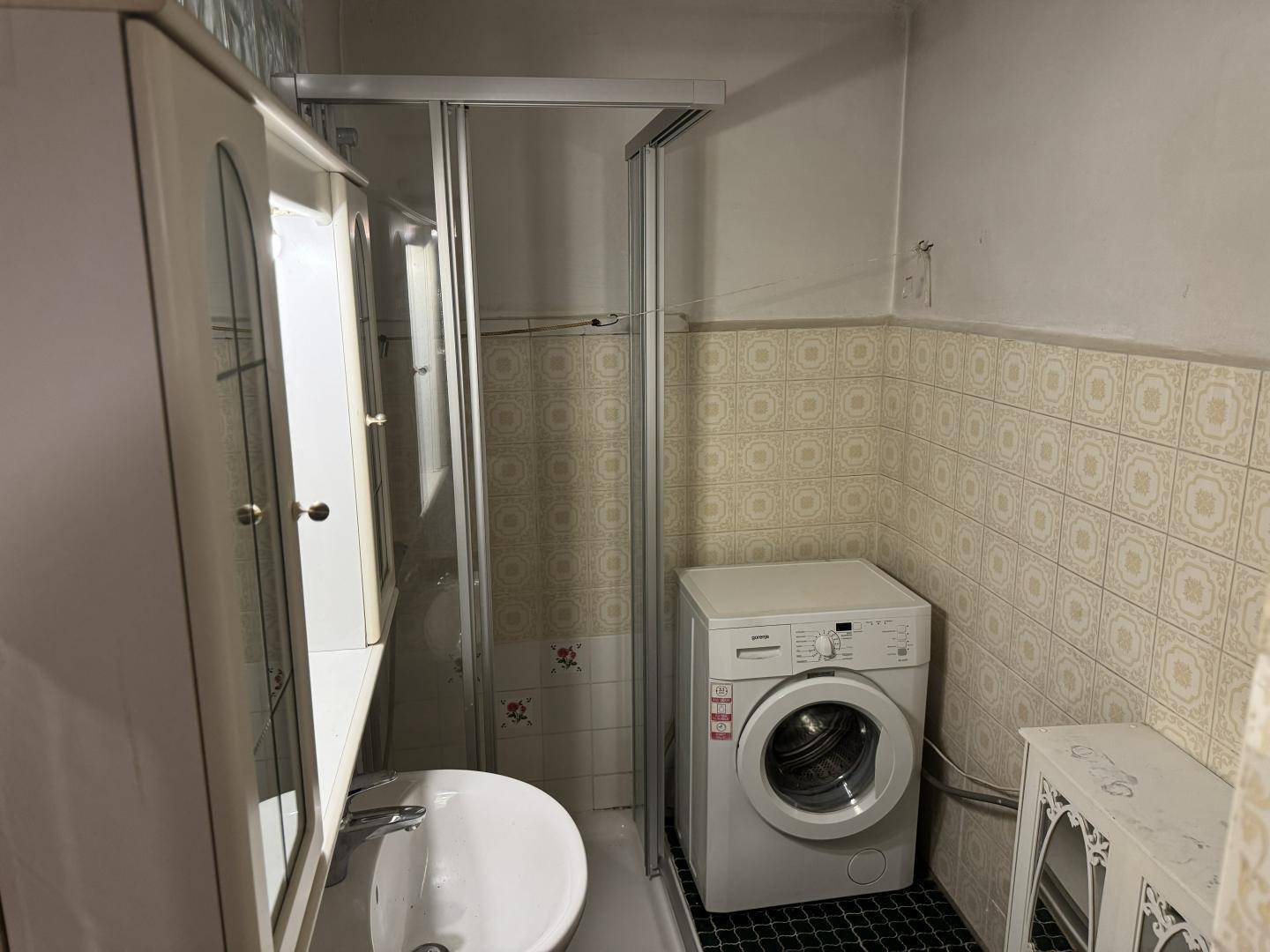 Badezimmer mit Duschkabine, Waschbecken und Waschmaschine, gefliest in traditionellem Stil.