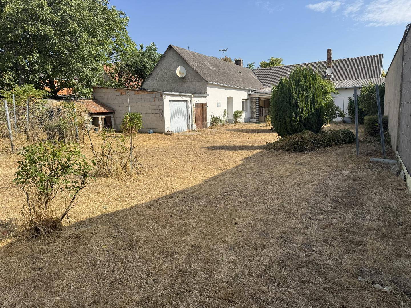 Weitläufiger, trockener Garten mit Nebengebäuden und Zaun im ländlichen Umfeld.