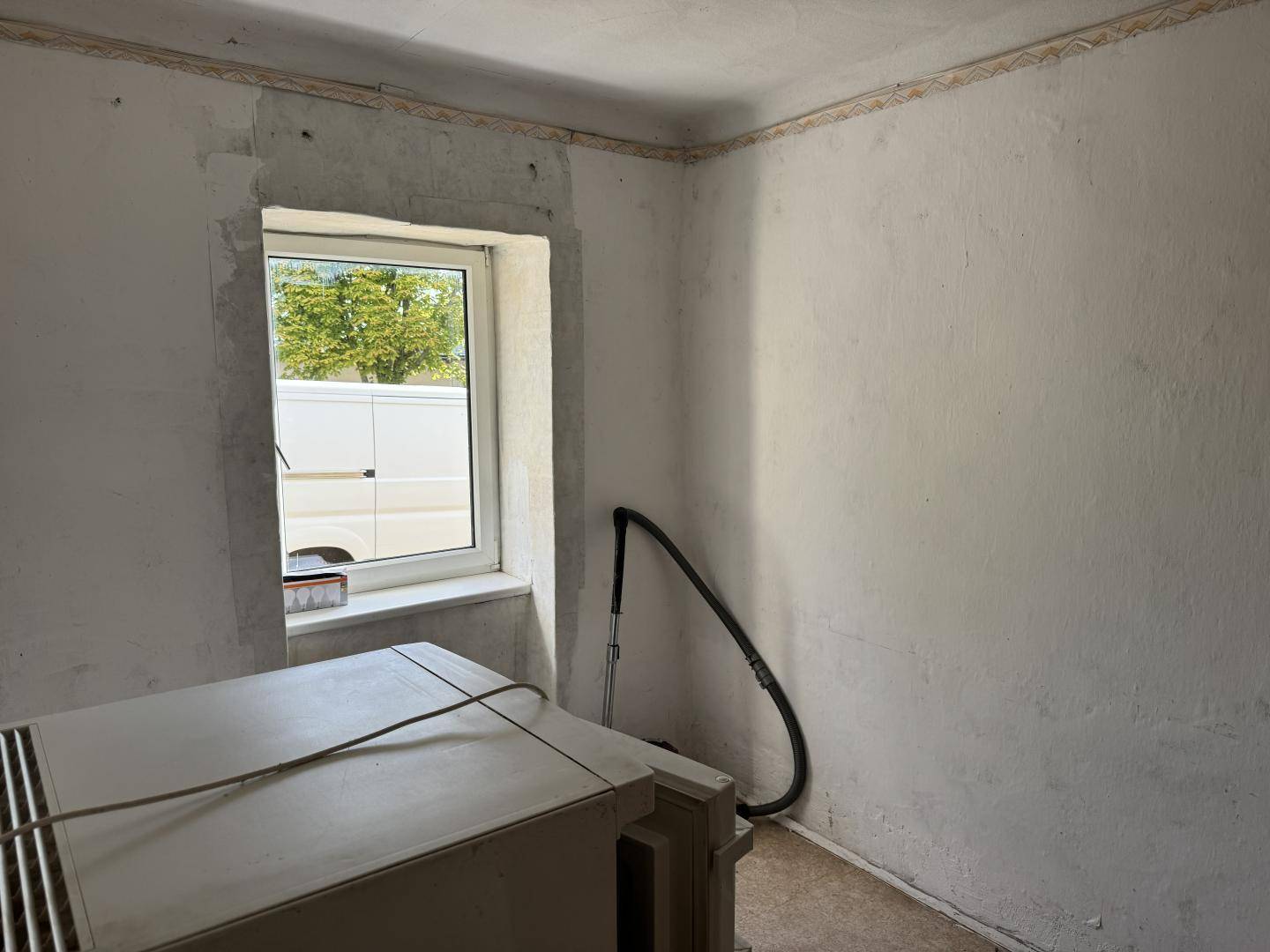 Leerer Raum mit weiß gestrichenen Wänden, einem Fenster und sichtbaren Renovierungsspuren.