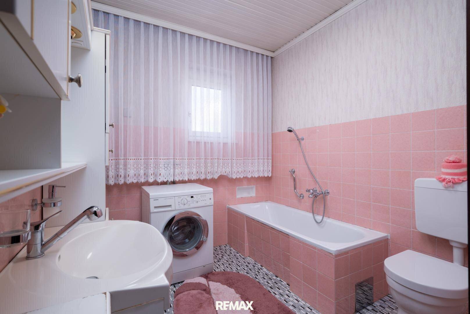 Badezimmer im 80er-Jahre-Stil mit rosa Fliesen, Badewanne und Waschmaschine.