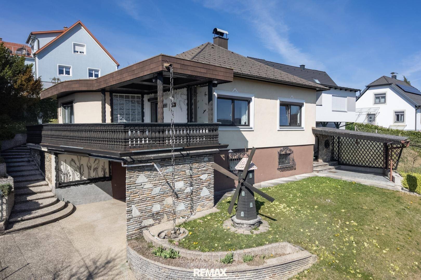 Rückansicht des Hauses mit Carport, Balkon und dekorativer Windmühle im Gartenbereich.