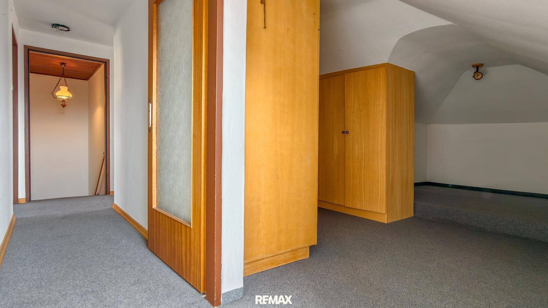 Flur im Dachgeschoss mit Teppichboden und Holzschränken, der zu weiteren Räumen führt.