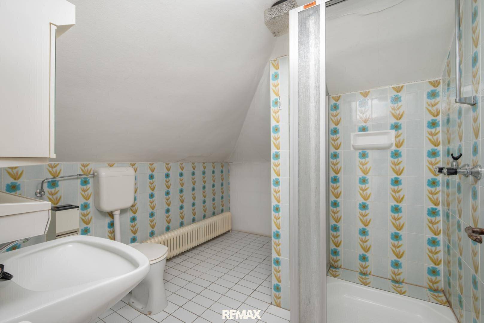 Badezimmer mit Dusche, WC und Waschbecken, ausgestattet mit gemusterten Fliesen im 80er-Jahre-Stil.